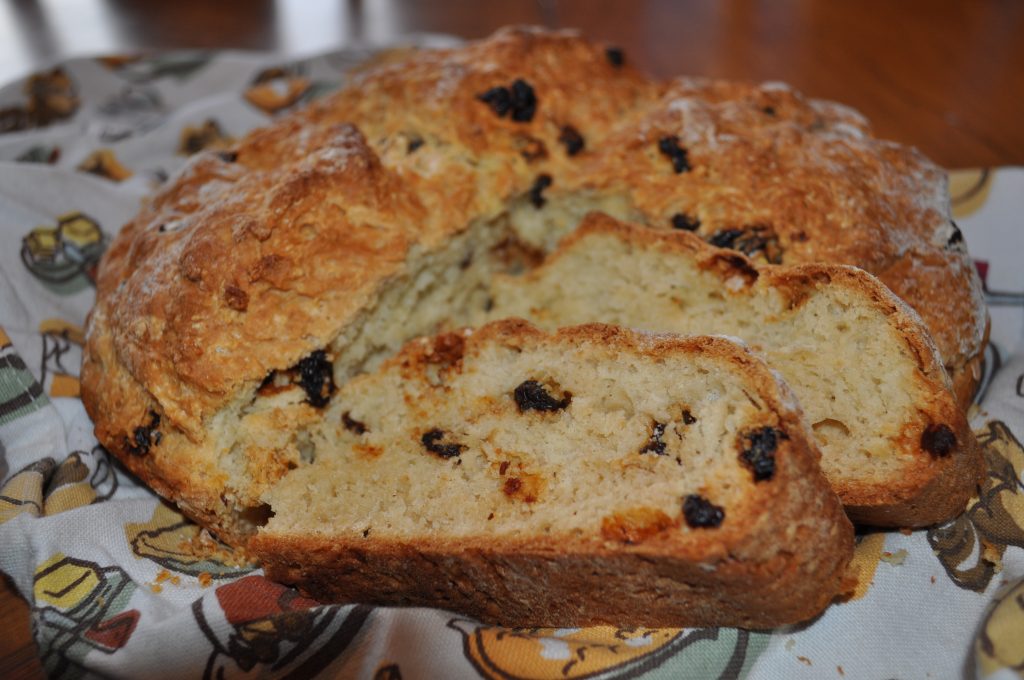 A loaf of raisin bread sliced open on a patterned cloth, golden-brown crust, warm tones, cozy homemade feel