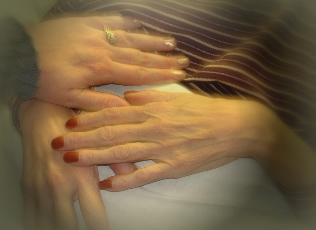 Two pairs of hands clasped together in a warm, intimate gesture, soft neutral tones